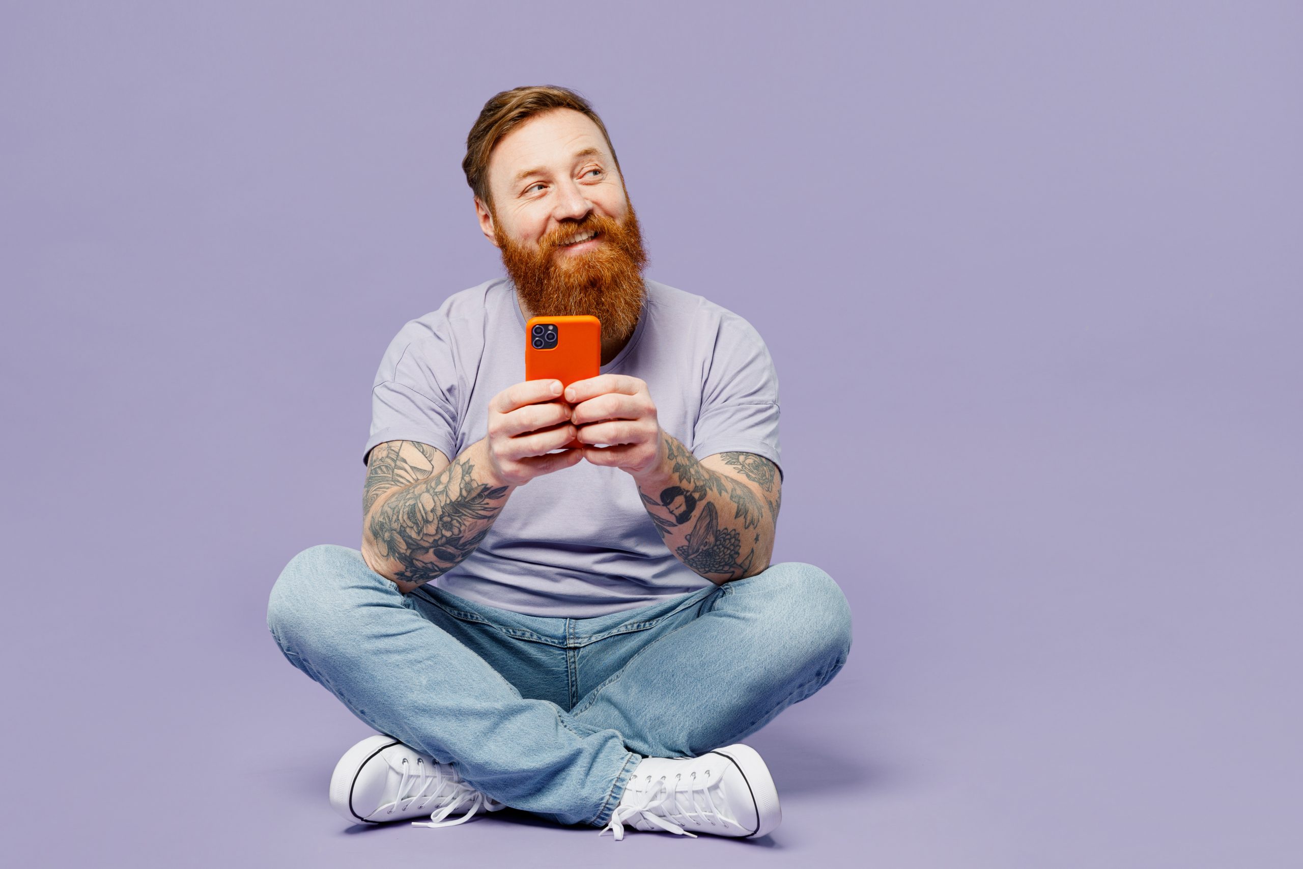 Homem sentado sorrindo olhando celular